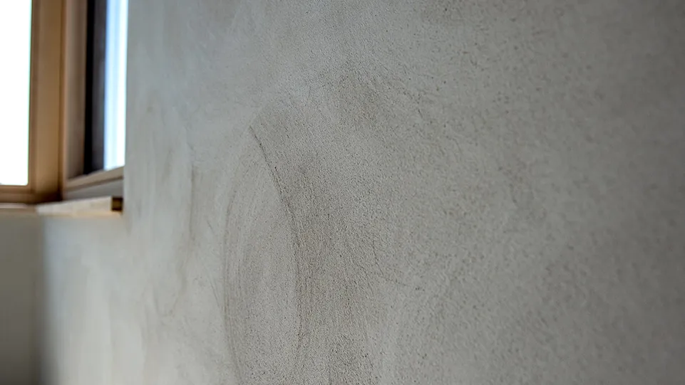 Fein gefilzte Lehmoberfläche in hellem Beige an einer Wand neben einem Fenster